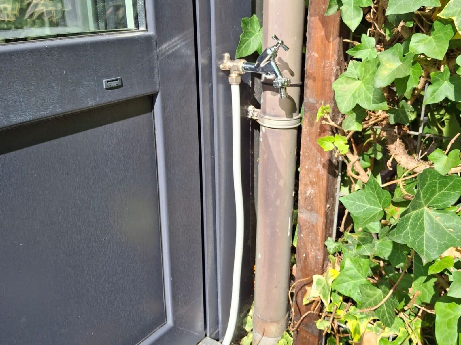 Buitenkraan aan de gevel naast een nieuw kozijn, met de leiding onder het kozijn doorgevoerd