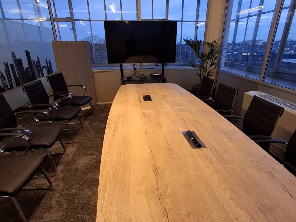 Vergaderruimte met een lange tafel met ingebouwde uitklapbare stopcontacten en een afbeelding op de ruit