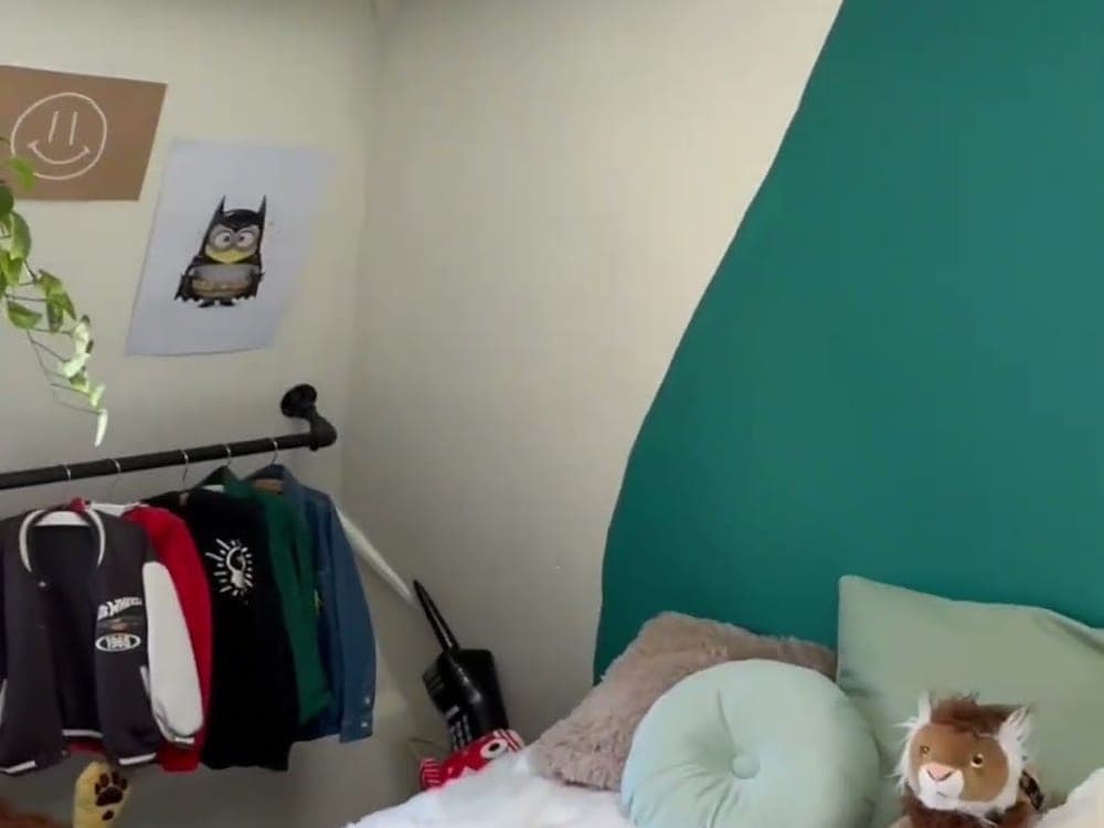 Kinderkamer met een zwart kledingrek van steigerbuis aan de muur, jasjes eraan en een bed met groene muur